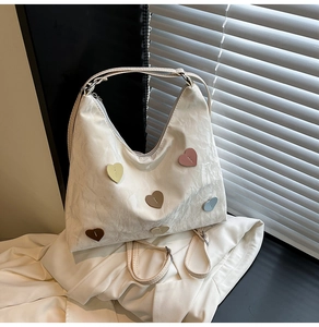 Detail of white wrinkled hobo bag featuring colorful heart patches and smooth zipper closure