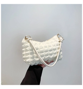 Detailed view of cream-white bubble-textured shoulder bag with gold metal rings