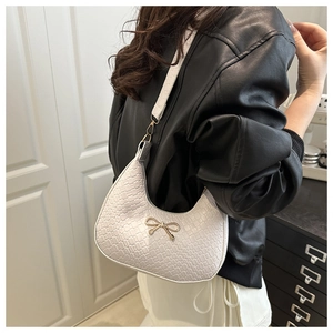 Detail of white crocodile pattern hobo bag with a gold bow buckle on model shoulder