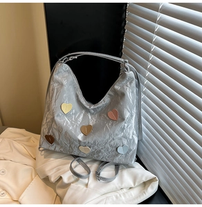 Detail of silver metallic pleated tote bag with colorful heart patches and long strap