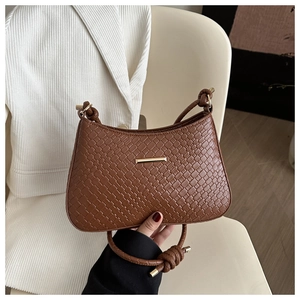 Close-up of a dark brown woven shoulder bag with golden metal bar on a beige chair