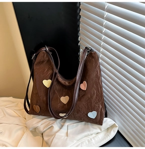 Detailed texture of dark brown pleated tote bag with colorful heart patches and strap
