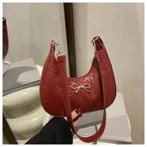 Detail of dark red woven crescent bag featuring a golden metal bow and wide shoulder strap