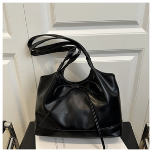 Détail d'un grand sac cabas noir en similicuir avec un nœud décoratif sur une chaise
