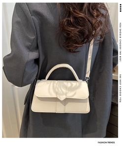 Detail of cream white handbag featuring a sharp flap design and slender crossbody strap