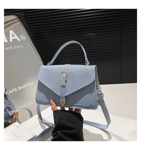 Detail of light blue denim textured flap handbag featuring a gold buckle and adjustable strap