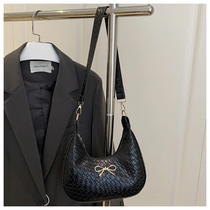 Detail of black woven crescent bag featuring a golden bow metal accessory and shoulder strap