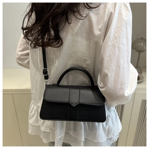 Model wearing a black leather crossbody bag with a top handle and adjustable strap