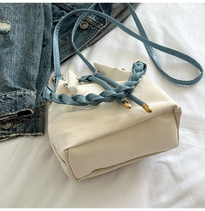 Top view of white bucket bag with blue woven handle and gold hardware on denim