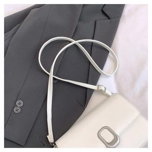 Close-up of white minimalist crossbody bag with silver oval hardware on a grey blazer