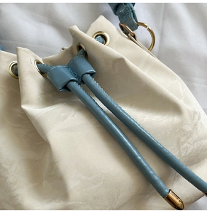 Detail of cream bucket bag showing light blue drawstrings and gold metallic eyelets