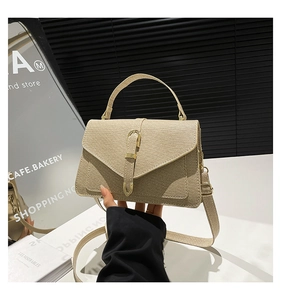 Detail of beige woven texture handbag with gold metal clasp and broad fabric strap