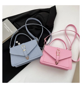 Detail of light blue and pink textured crossbody bags with gold buckles on a suit background