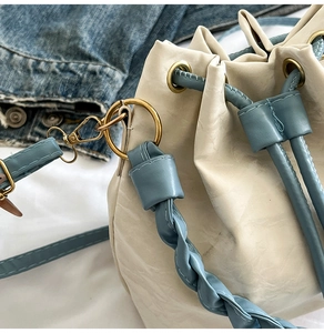 Detail of cream bucket bag with blue woven leather strap and golden metal ring hardware