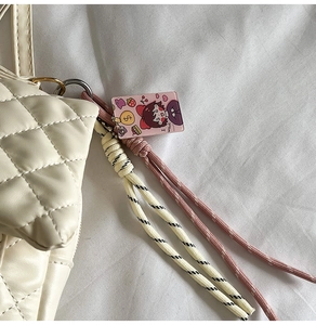 Close-up of cream quilted bag with stylish pink woven charm and acrylic strawberry tag
