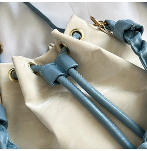 Detailed macro view of cream PU leather bucket bag with blue drawstring and gold eyelets