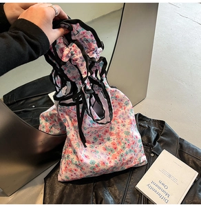 Detail of pink floral drawstring bag with black ribbon closure on dark leather background