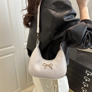 White crocodile-textured half-moon shoulder bag with a gold bow buckle on black leather jacket