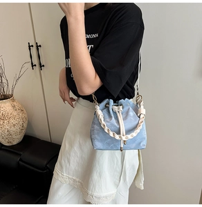 Detail of light blue drawstring bucket bag with white woven handle and gold hardware detail