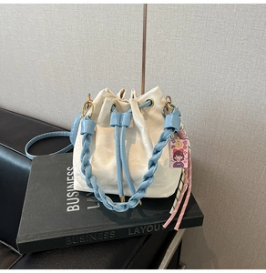 Close-up of creamy white pleated bucket bag with blue woven handle and gold hardware detail