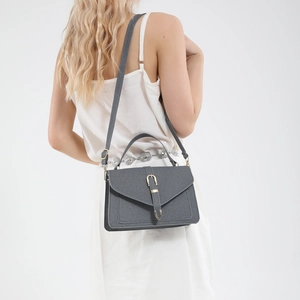 Minimalist grey crossbody bag with denim texture and gold U-shaped buckle on white dress
