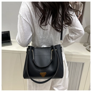 Detail of matte black bucket bag showing U-shaped gold handle and metal triangle plaque