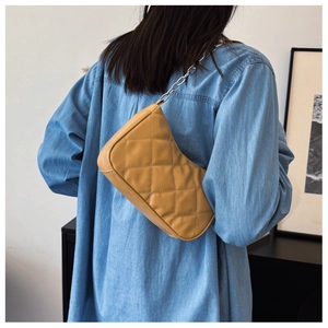 Detail of yellow quilted shoulder bag with silver chain strap worn over denim shirt