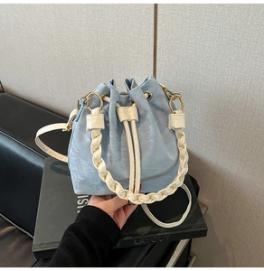 Close-up of light blue drawstring bucket bag featuring a cream braided handle detail