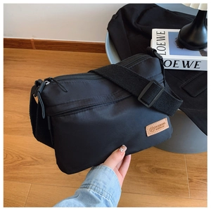 Close-up of black nylon crossbody bag with multi-zipper pockets and leather patch detail