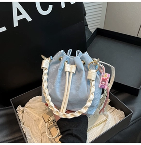 Close-up of light blue bucket bag with woven handle and pink cartoon charm detail