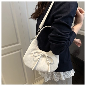 Detail of cream half-moon underarm bag with large bow decoration and silver metal hook