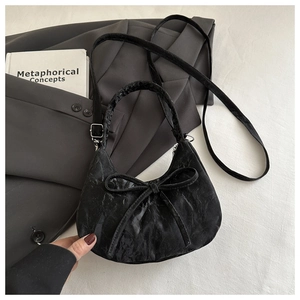 Close-up of black pleated velvet handbag with a large decorative bow on a blazer