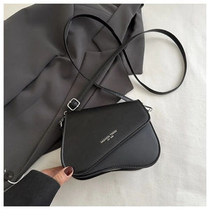 Detail of minimalist black leather crossbody bag with asymmetric flap and silver lettering