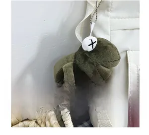Detail view of military green plush charm with X-shaped embroidery on a white backpack