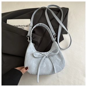 Close-up of light blue pleated hobo bag featuring bow detail and textured synthetic leather