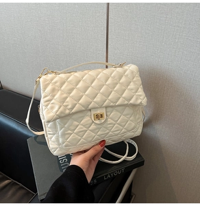 Close-up of white quilted tote bag featuring golden twist lock and metallic chain strap