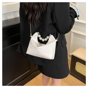 Detailed view of a white leather crossbody bag featuring a large faux pearl top handle