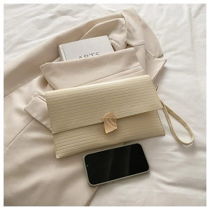 Detail of beige pleated clutch bag with gold buckle and wrist strap on suit blazer