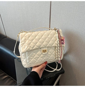 Detail of off-white quilted tote bag featuring golden turn-lock and woven accessory