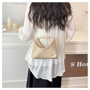 Detail of beige shoulder bag featuring oversized pearls on handle and gold chain strap
