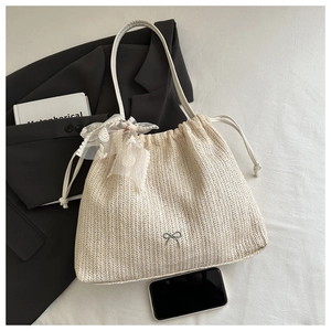 Detail of cream woven tote bag with lace bow and silver butterfly pendant on fabric