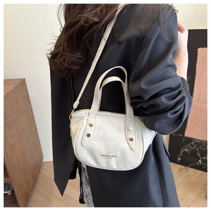 Sac bandoulière beige avec rivets et lettrage porté sur une veste de costume noire
