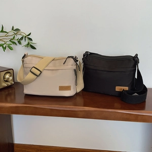 Minimalist nylon crossbody bags in beige and black with multi-zipper layers on a wooden table