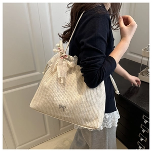 Close-up of beige woven tote bag with lace bow and metal butterfly pendant accessory