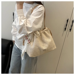 Detail of straw woven tote bag featuring floral embroidery, lace trim and drawstring closure