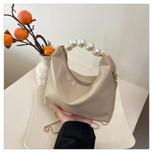 Detail of elegant beige crescent bag with a decorative faux pearl handle and gold hardware