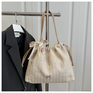 Detail of woven straw tote bag with metal bow accent and floral lace ribbon on leather handle