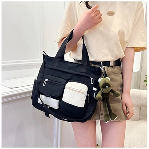 Detail of black multi-pocket canvas tote bag featuring white contrast zippers and frog pendant