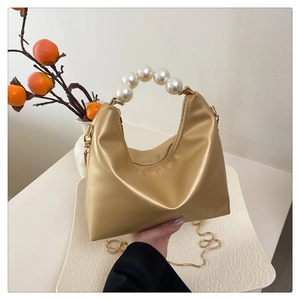 Close-up of champagne gold half-moon handbag featuring elegant large pearl handle and gold chain
