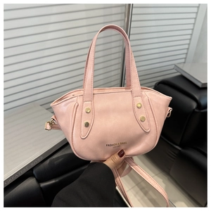 Detail of pink leather handbag with gold rivets and adjustable shoulder strap held by hand